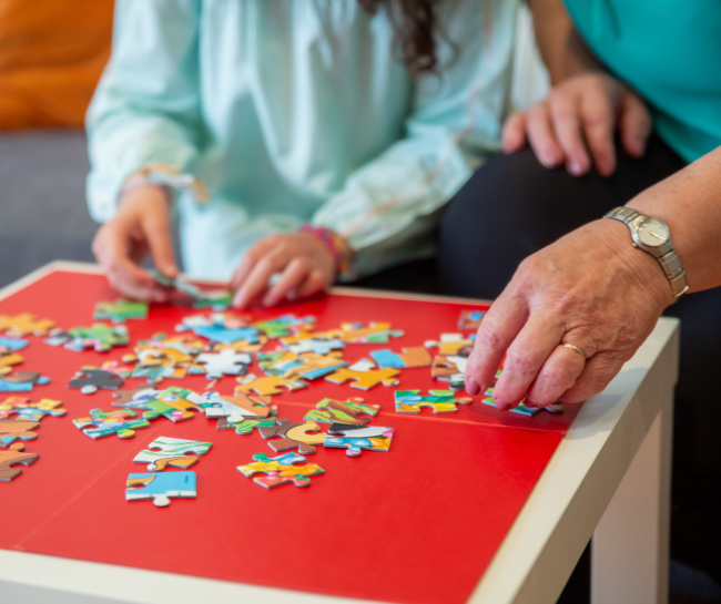 Stół pełny puzzli i nie pełny widok dwóch osób