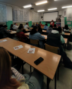 Sala w której jest młodzież oraz przedstawiciel uczelni oraz kadra BCU. Uczniowie siedzą w ławach. Na tle przedstawiciela uczelni znajduje się rzutnik, rollup uczelni oraz BCU