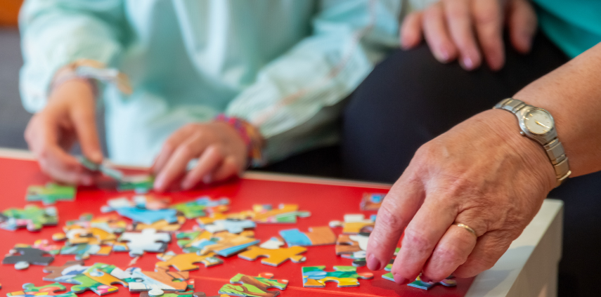 Stół pełny puzzli i nie pełny widok dwóch osób